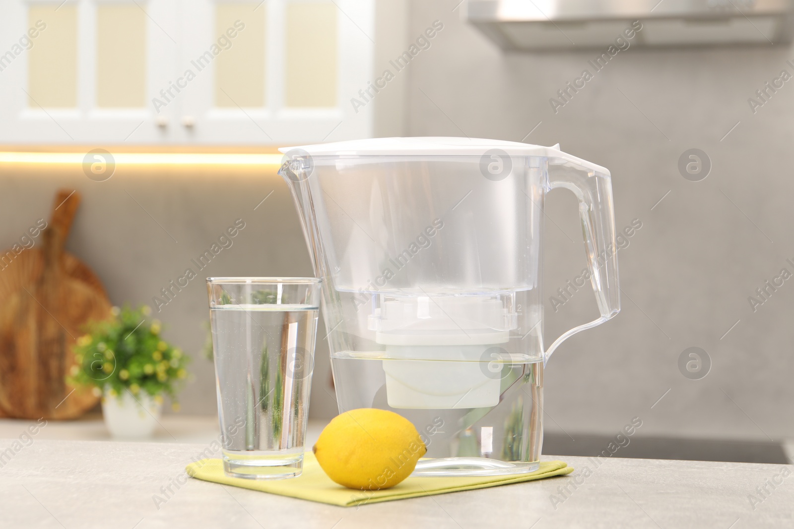 Photo of Water filter jug, glass and lemon on light grey table in kitchen