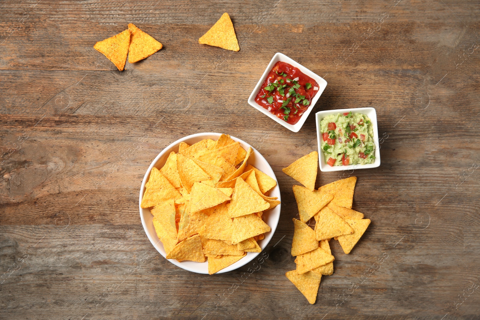 Photo of Bowl of delicious mexican nachos chips and sauces on wooden table, flat lay