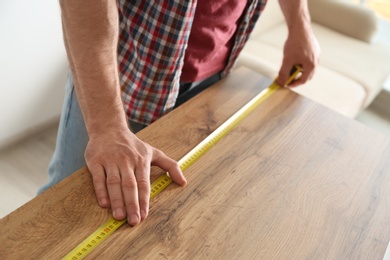 Man measuring wooden table, closeup. Construction tool