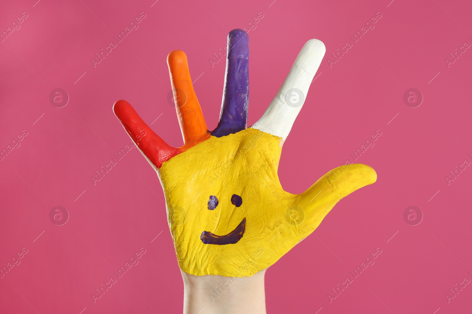 Photo of Kid with smiling face drawn on palm against pink background, closeup