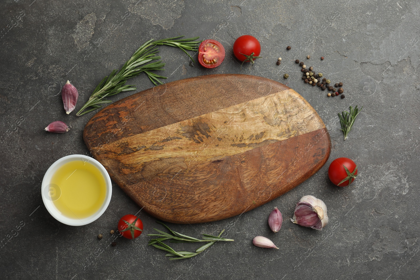 Photo of Cutting board, rosemary, garlic, oil and tomatoes on black table, flat lay. Space for text