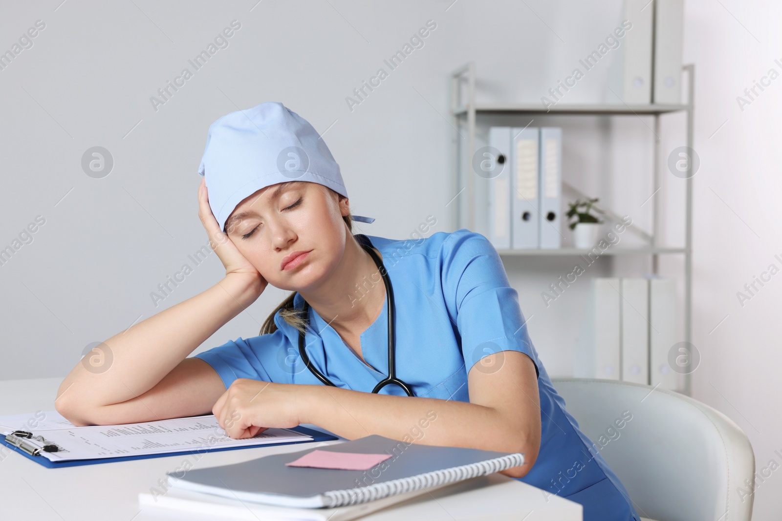 Photo of Tired young doctor sleeping at workplace in office