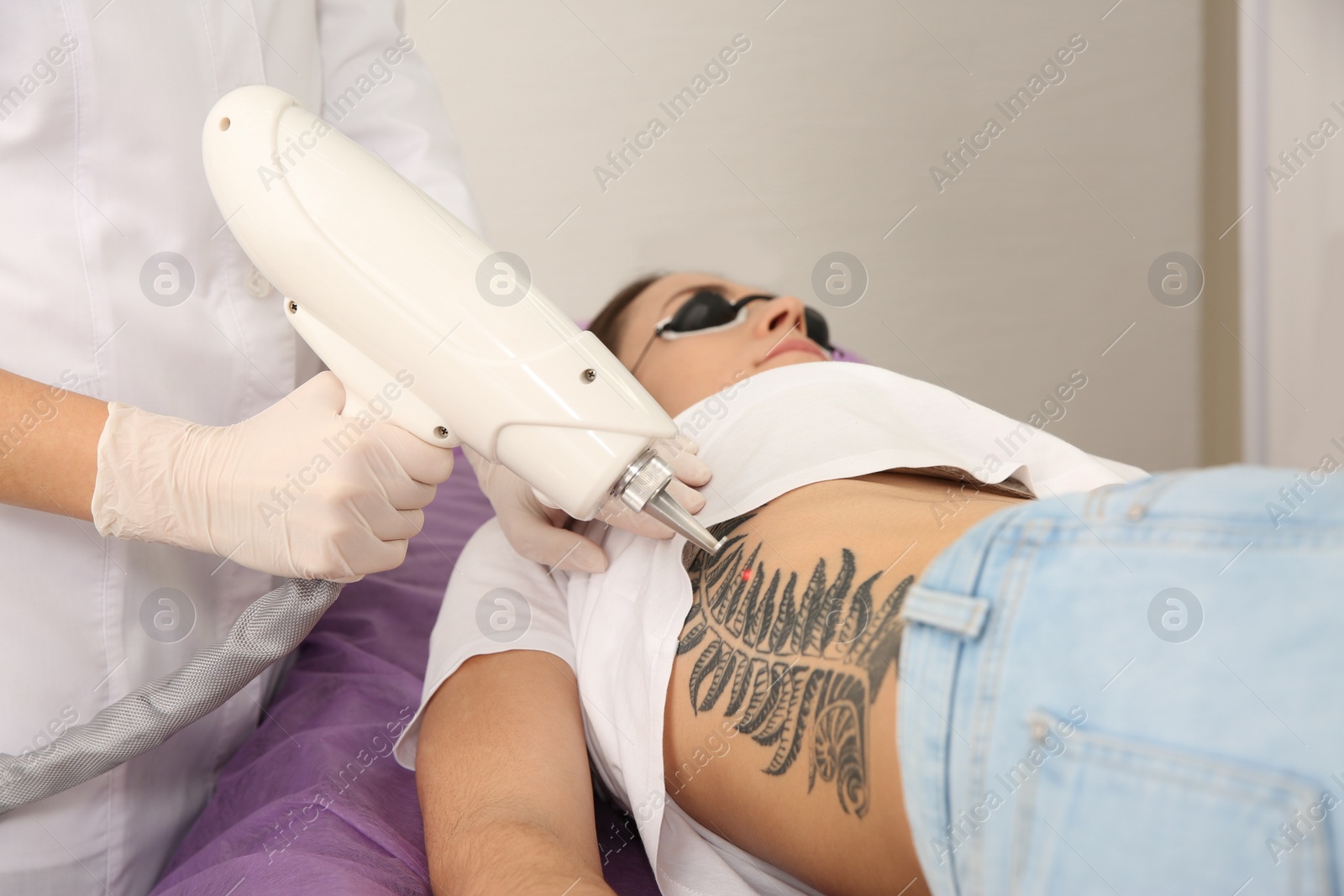 Photo of Young woman undergoing laser tattoo removal procedure in salon