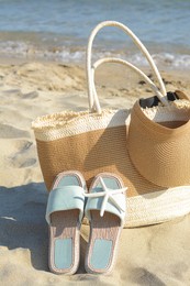 Stylish bag with slippers, visor cap and dry starfish on sandy beach near sea