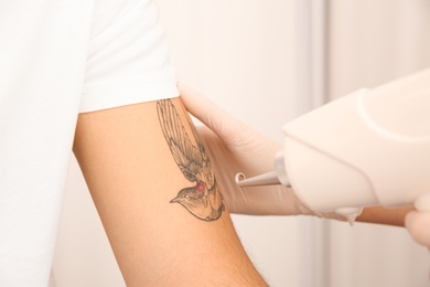 Photo of Young man undergoing laser tattoo removal procedure in salon, closeup