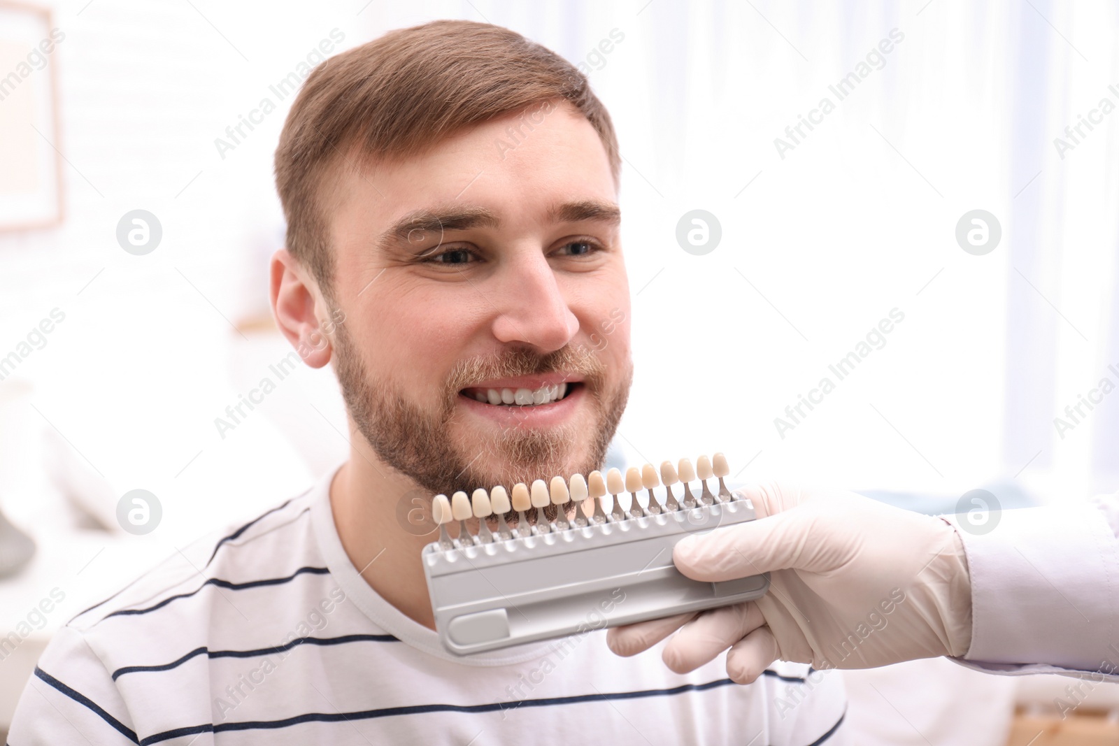 Photo of Dentist checking young man's teeth color in dental office