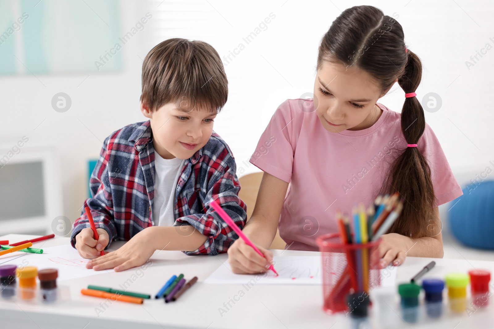 Photo of Happy brother and sister drawing at white table in room