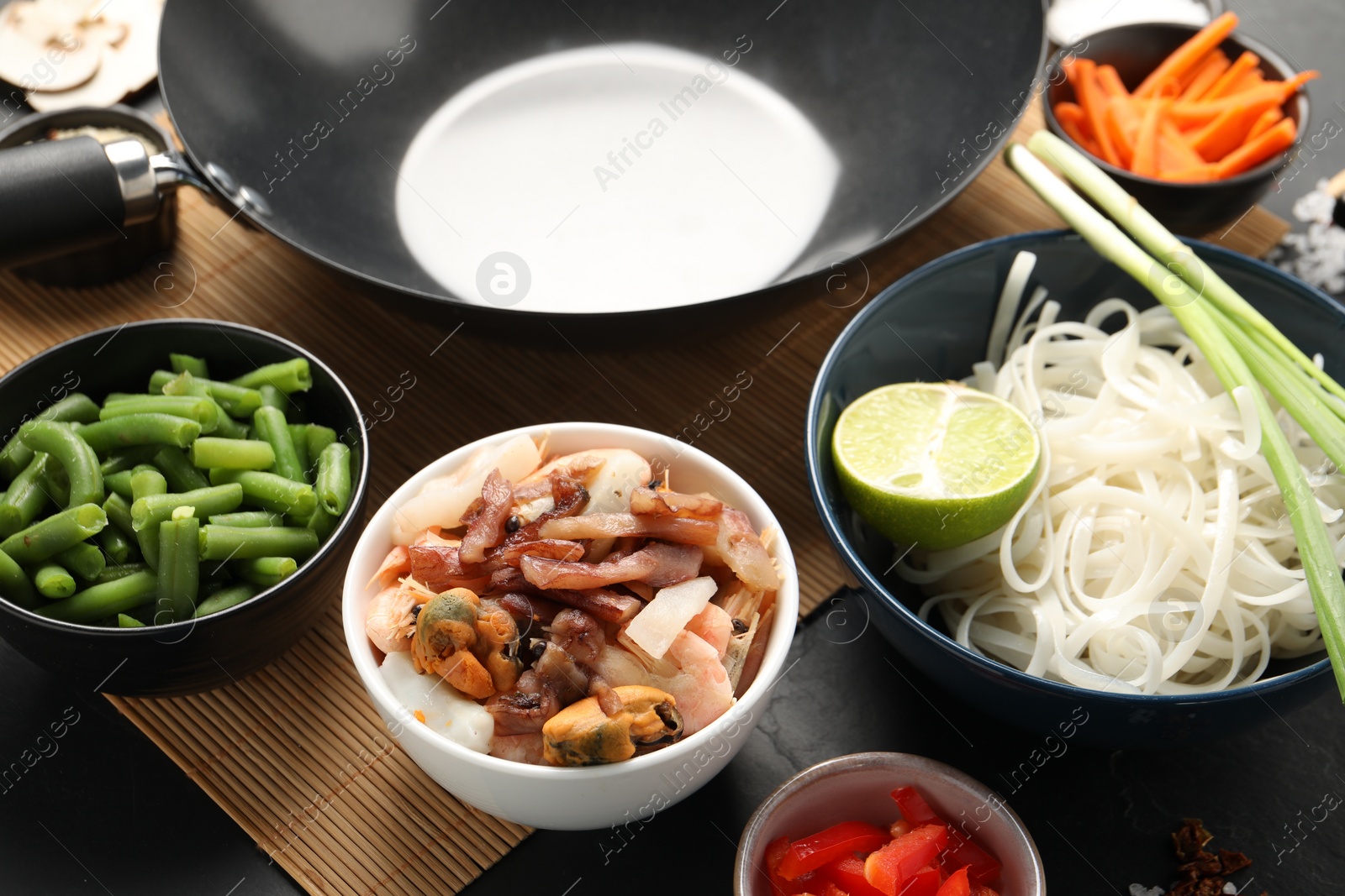 Photo of Black wok and products on dark table, closeup