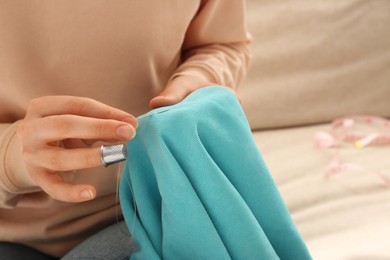 Photo of Woman sewing on turquoise fabric with thimble and needle indoors, closeup. Space for text