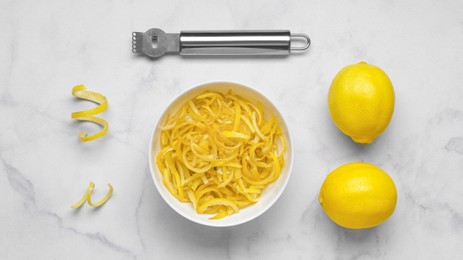 Photo of Bowl with peel pieces, fresh lemons and zester on white marble table, flat lay