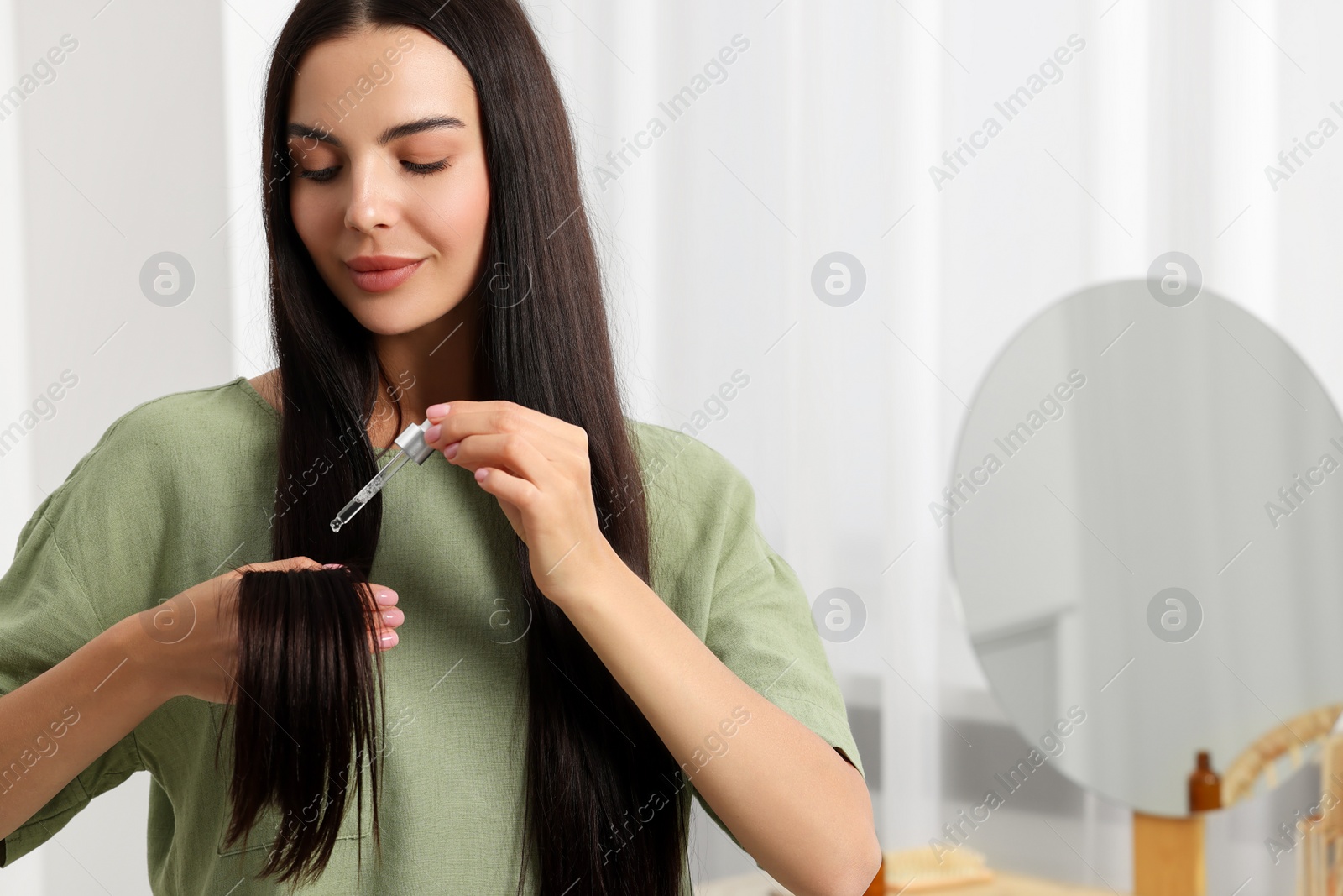 Photo of Beautiful woman applying hair serum in room, space for text. Cosmetic product