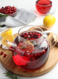 Photo of Tasty hot cranberry tea with lemon, rosemary and fresh berries in teapot on white table