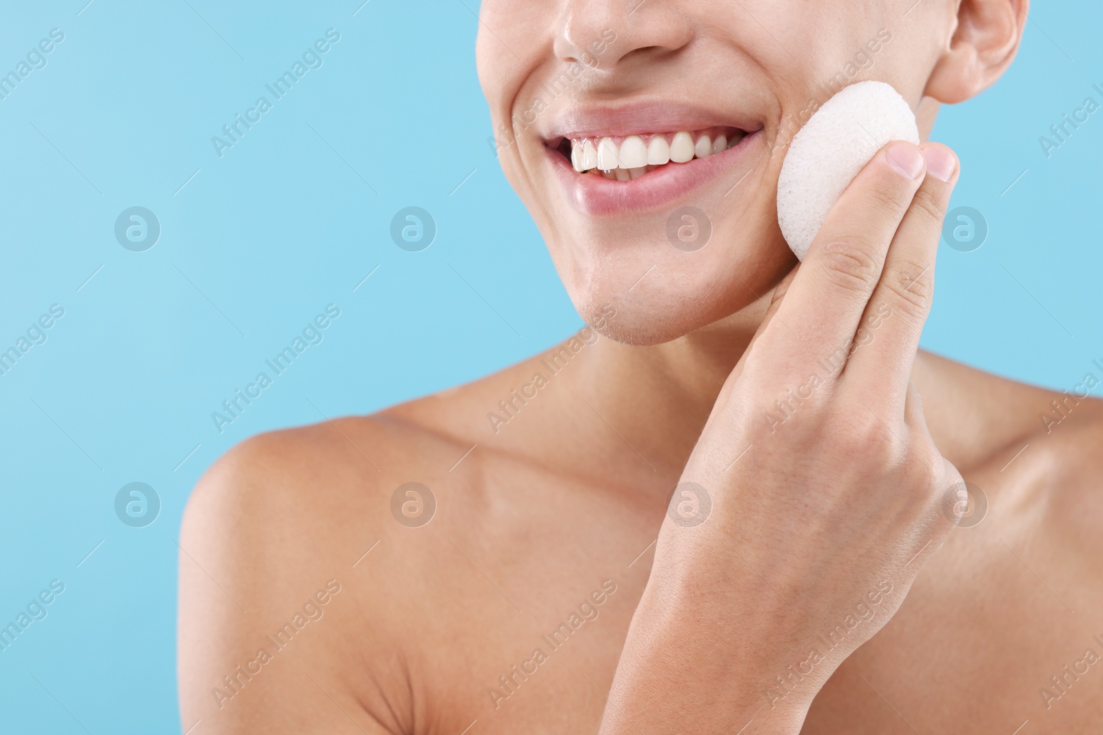 Photo of Happy young man washing his face with sponge on light blue background, closeup