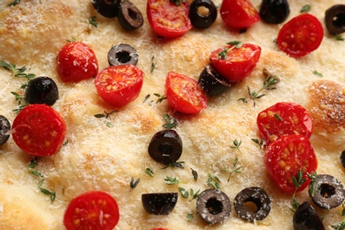 Traditional Italian focaccia bread with olives, cheese, tomatoes and thyme as background, closeup