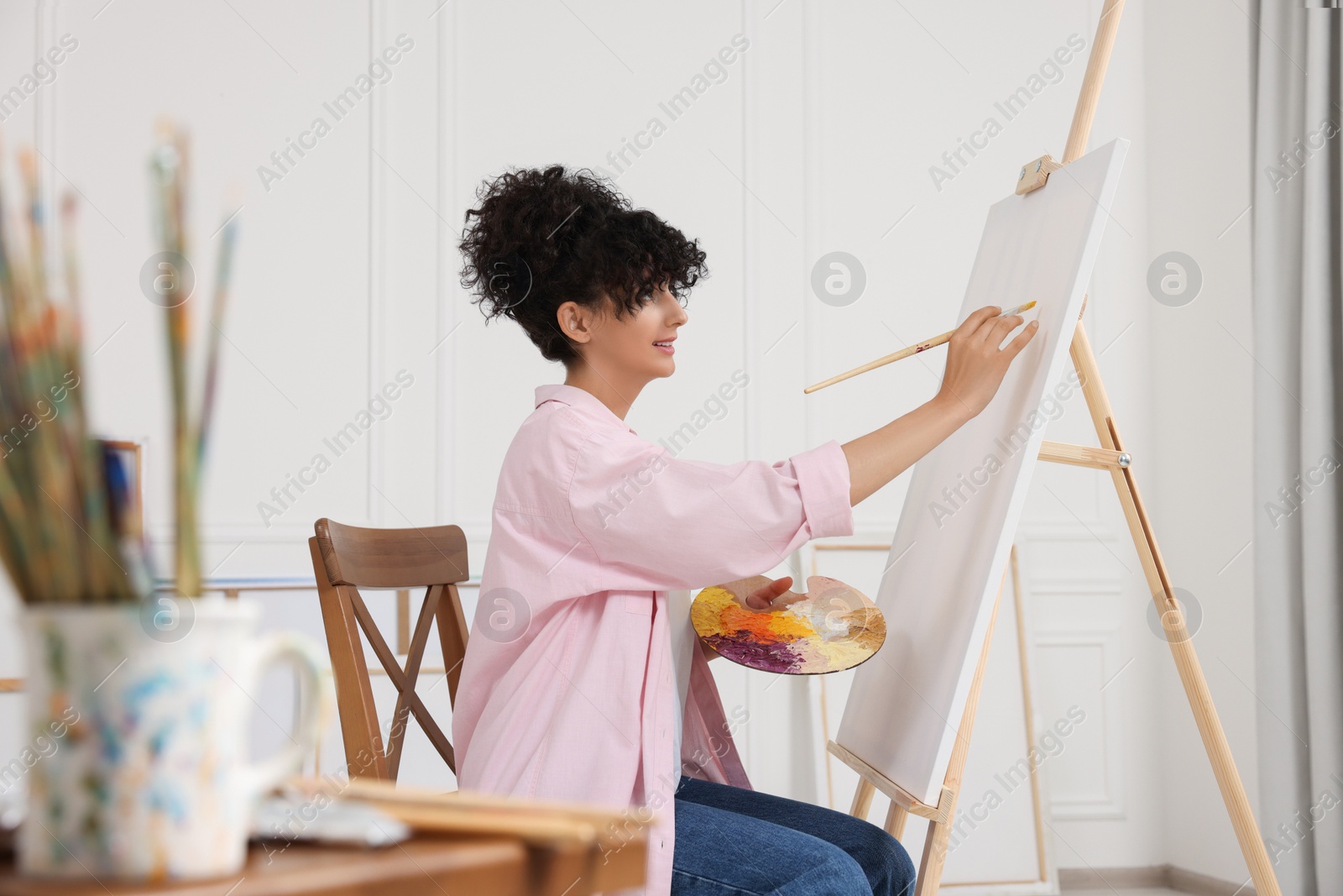 Photo of Young woman painting on easel with canvas in studio