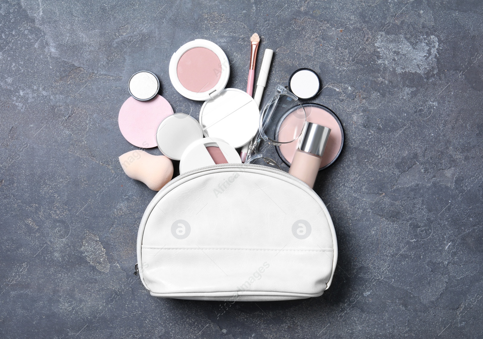 Photo of Cosmetic bag with makeup products and beauty accessories on grey stone background, flat lay
