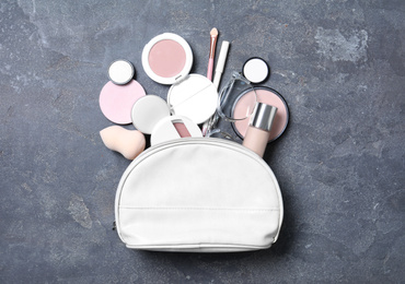 Photo of Cosmetic bag with makeup products and beauty accessories on grey stone background, flat lay