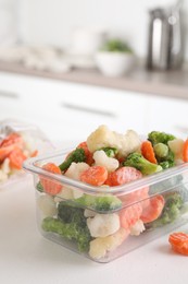 Photo of Mix of different frozen vegetables in plastic container on white textured table in kitchen, closeup. Space for text