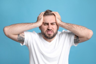 Photo of Young man suffering from headache on light blue background