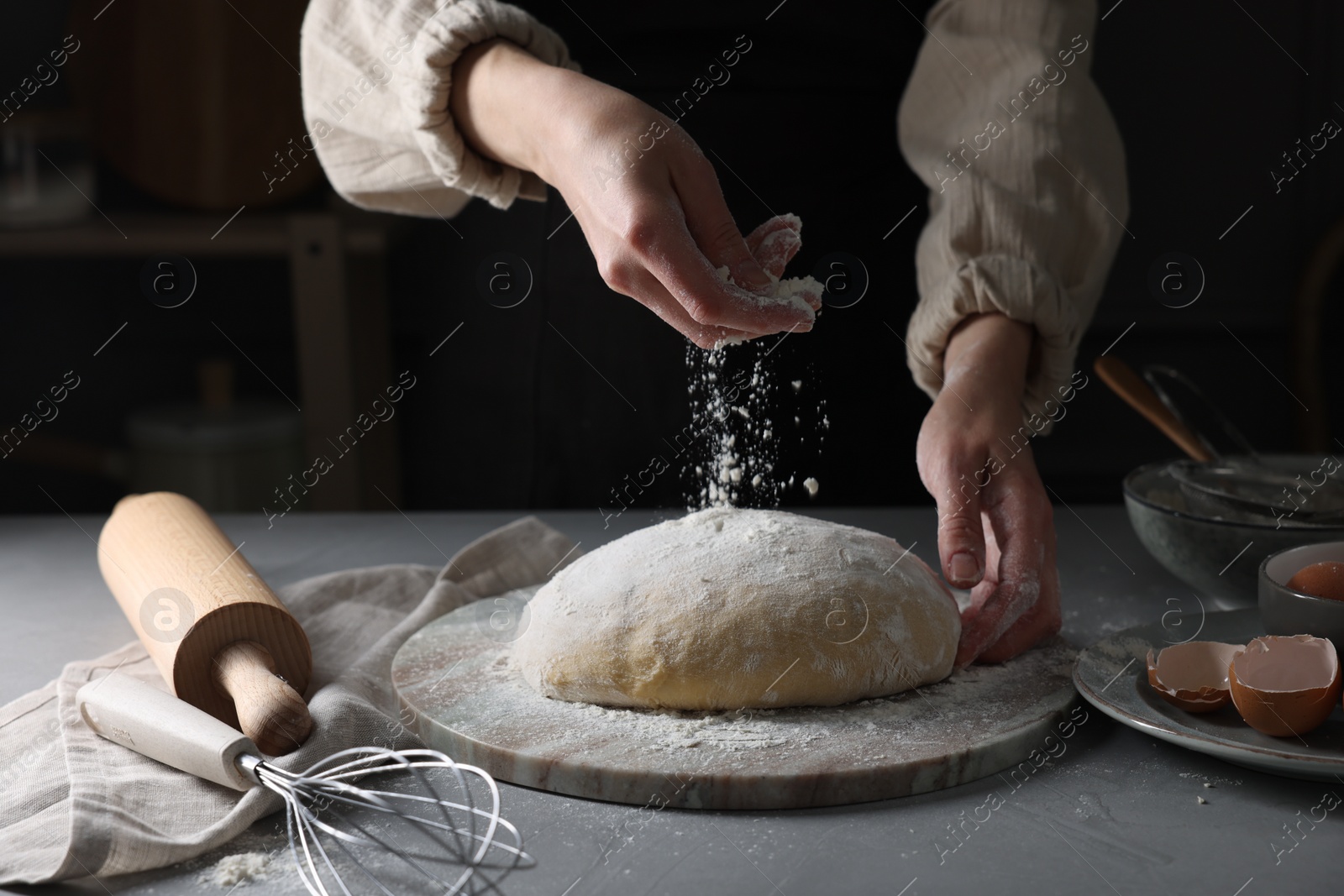Photo of Making dough. Woman adding flour at grey table, closeup
