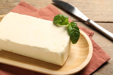 Block of tasty butter with basil and knife on wooden table, closeup