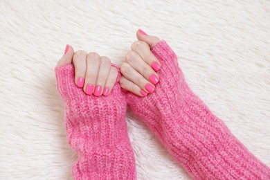 Photo of Woman showing her manicured hands with pink nail polish on faux fur mat, top view