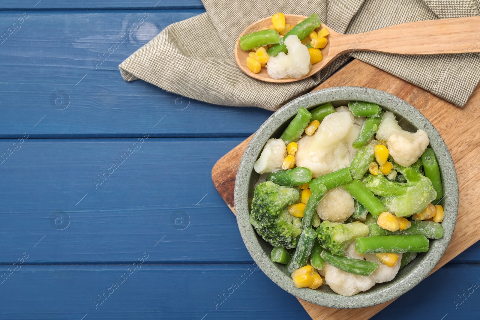 Photo of Mix of different frozen vegetables in bowl on blue wooden table, top view. Space for text