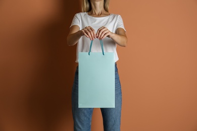 Photo of Woman with paper shopping bag on light brown background, closeup