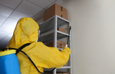 Pest control worker spraying pesticide on rack indoors