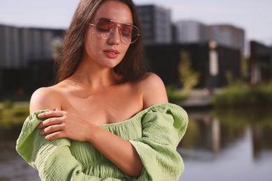 Beautiful woman in sunglasses near river, space for text