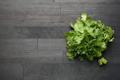 Photo of Bunch of fresh coriander on black wooden table, top view. Space for text