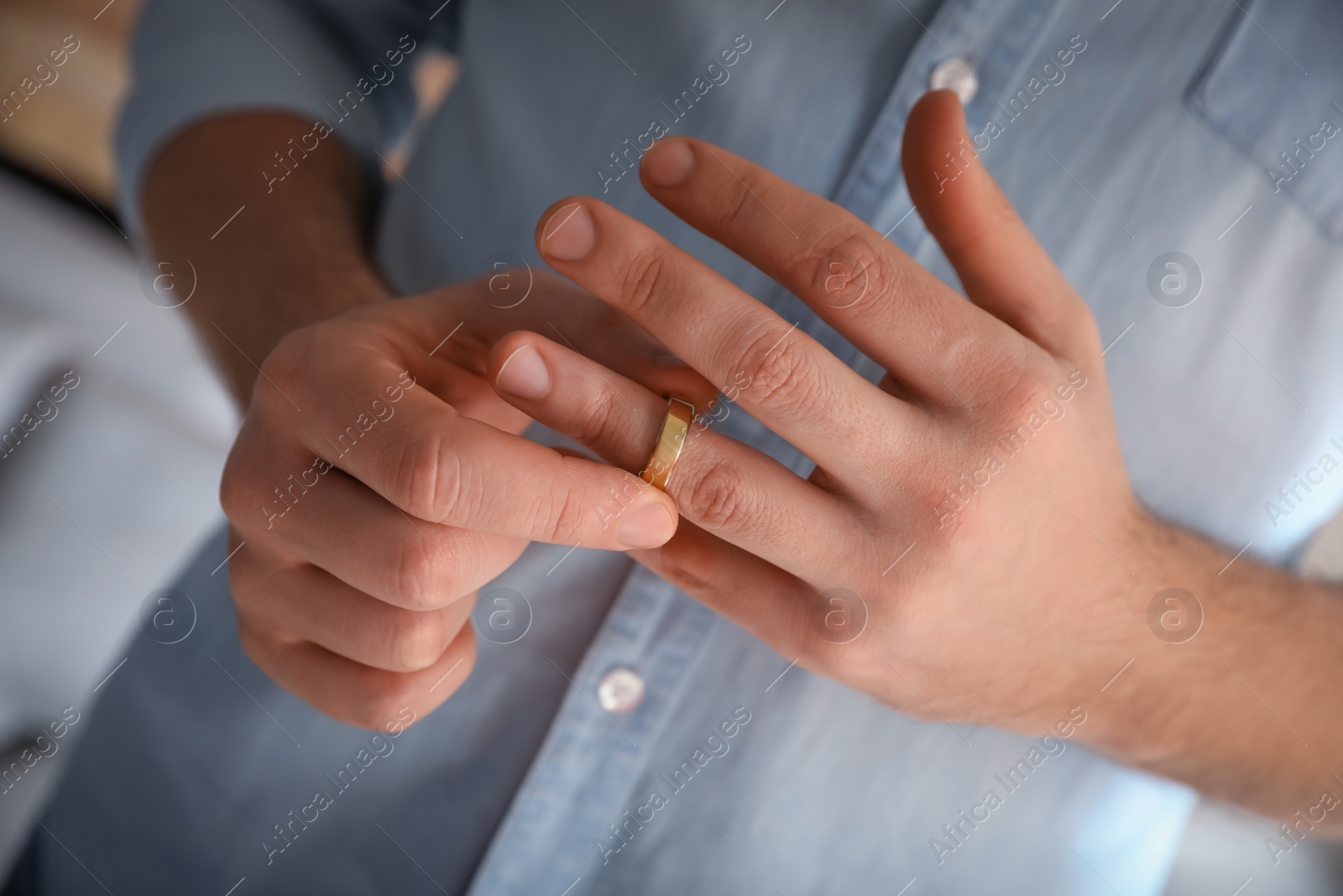 Photo of Man taking off wedding ring on blurred background, closeup. Divorce concept