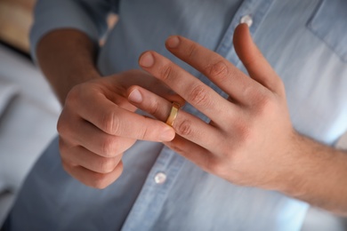 Man taking off wedding ring on blurred background, closeup. Divorce concept