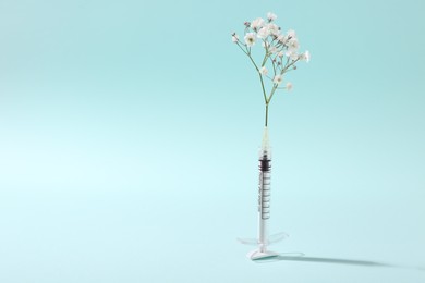 Photo of Cosmetology. Medical syringe and gypsophila on light blue background, space for text