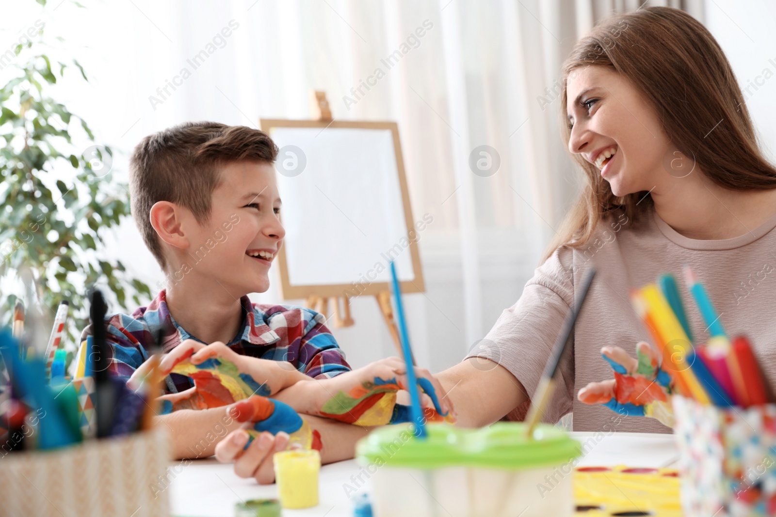 Photo of Young woman with child painted hands at table indoors