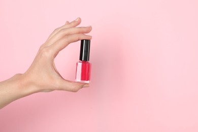 Photo of Woman holding nail polish on pink background, closeup. Space for text