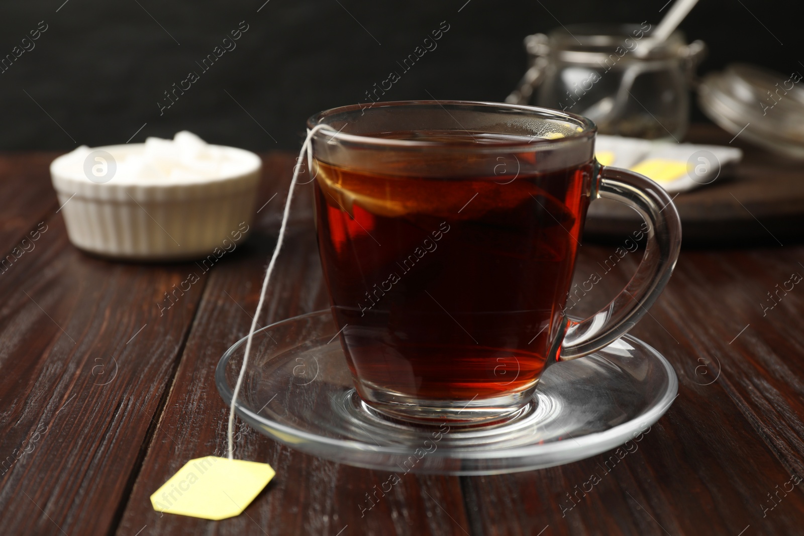 Photo of Brewing tea. Glass cup with tea bag on wooden table, closeup