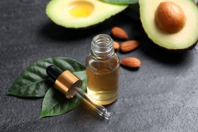 Photo of Essential oil, avocado and almonds on black table