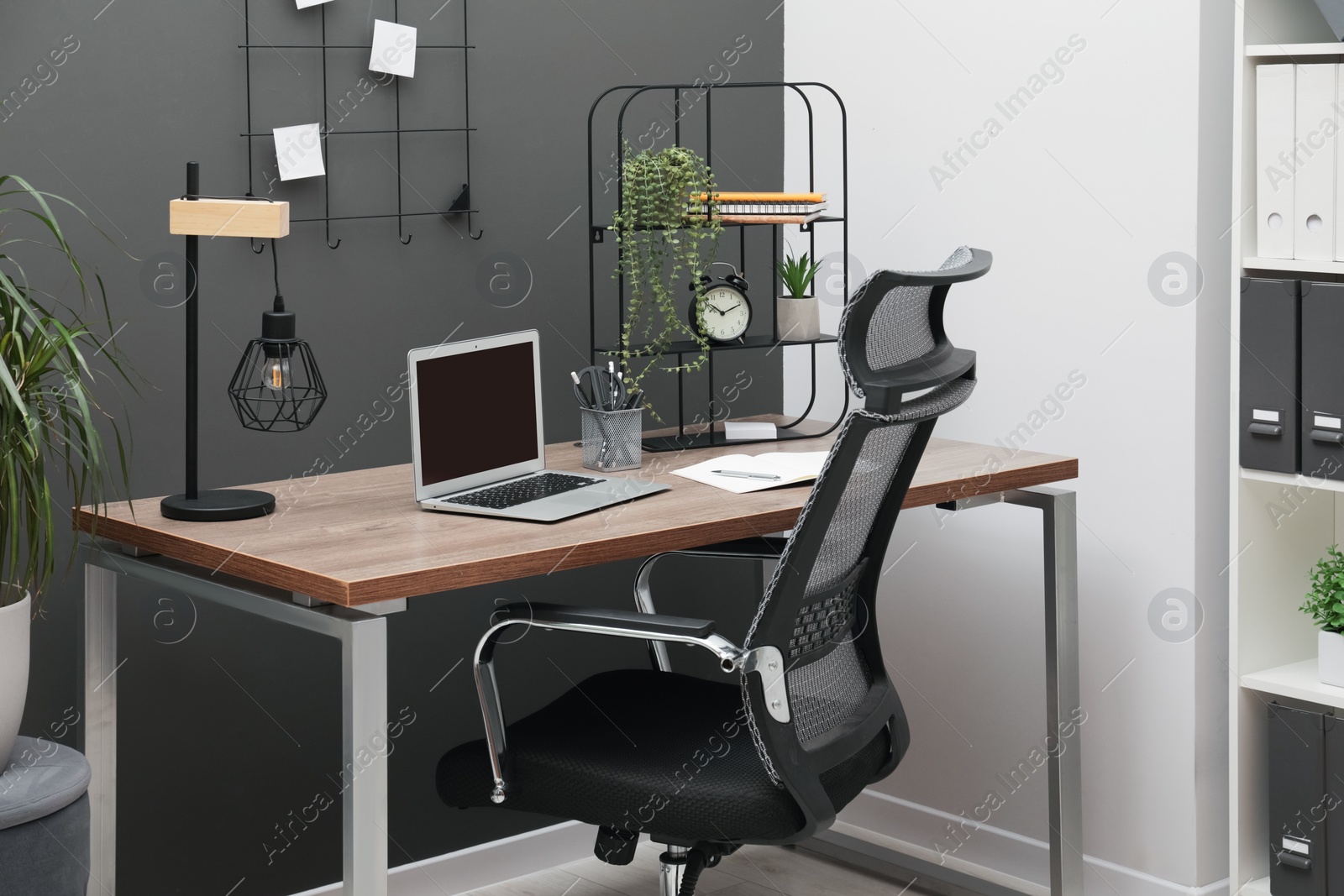 Photo of Cozy workplace with modern laptop on desk and comfortable chair at home