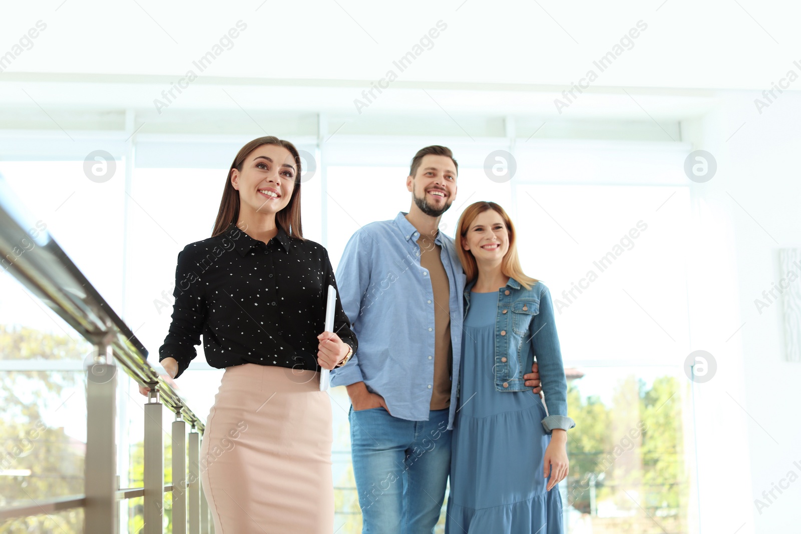 Photo of Female real estate agent showing new house to couple, indoors
