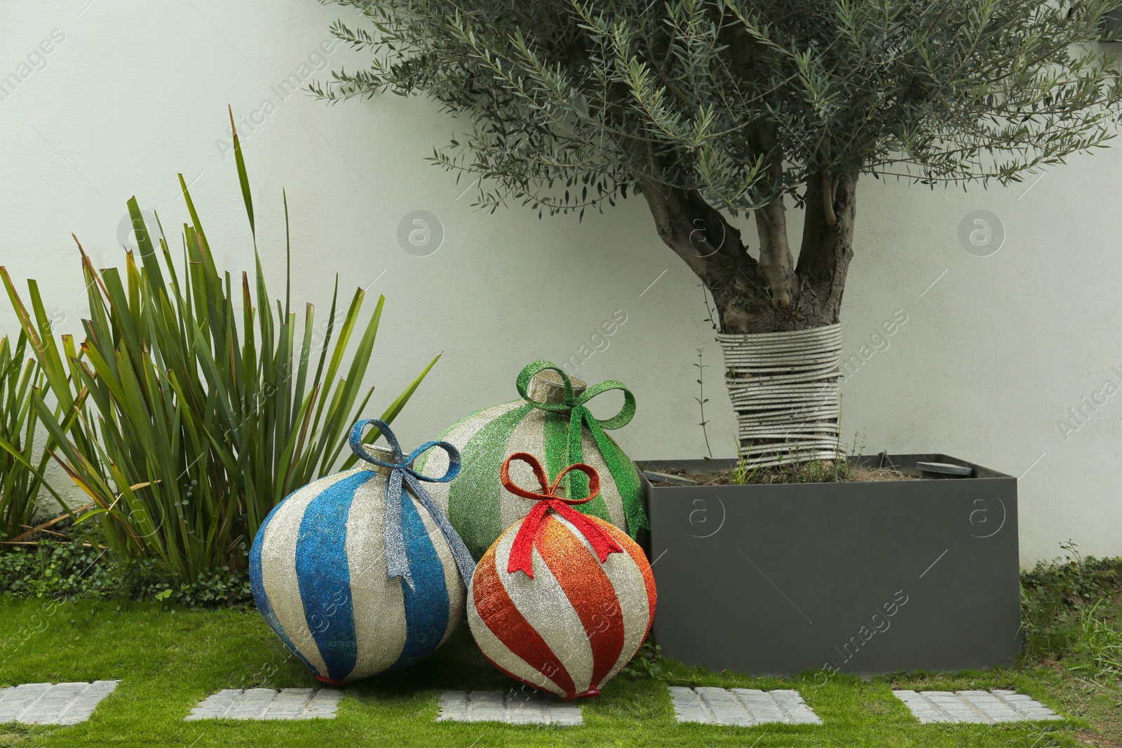 Photo of Beautiful shiny Christmas baubles on green grass outdoors. Festive street decorations