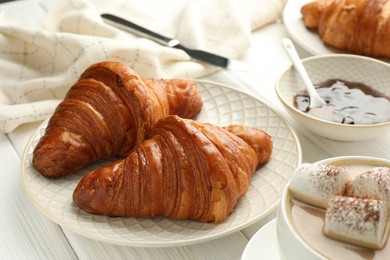 Plate with tasty croissants served on white wooden table, closeup