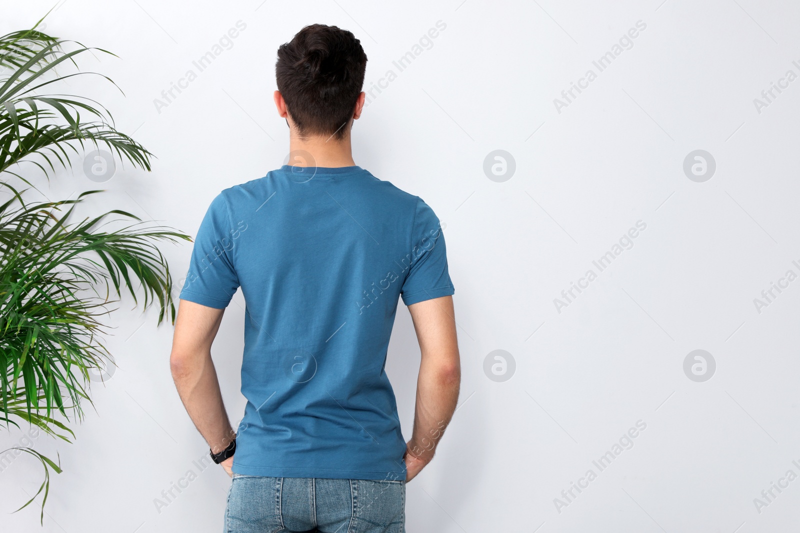 Photo of Young man in t-shirt near light wall. Mock up for design