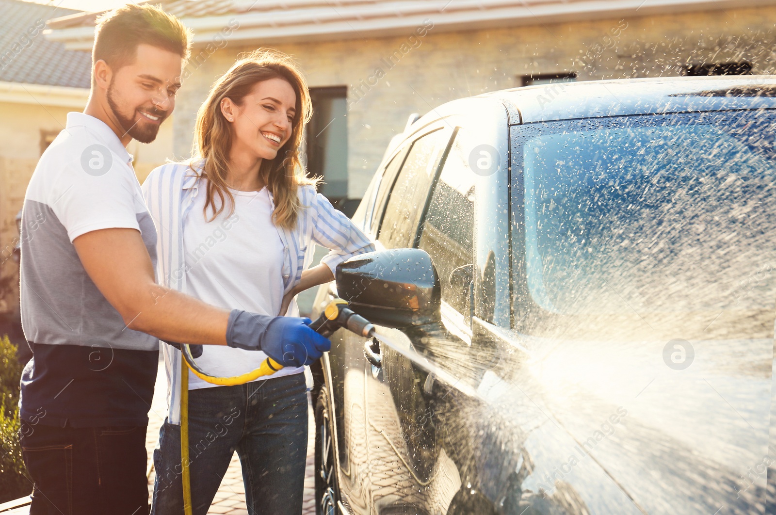 Photo of Happy young couple washing car at backyard on sunny day