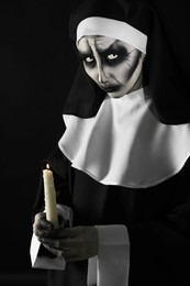 Photo of Scary devilish nun with burning candle on black background. Halloween party look