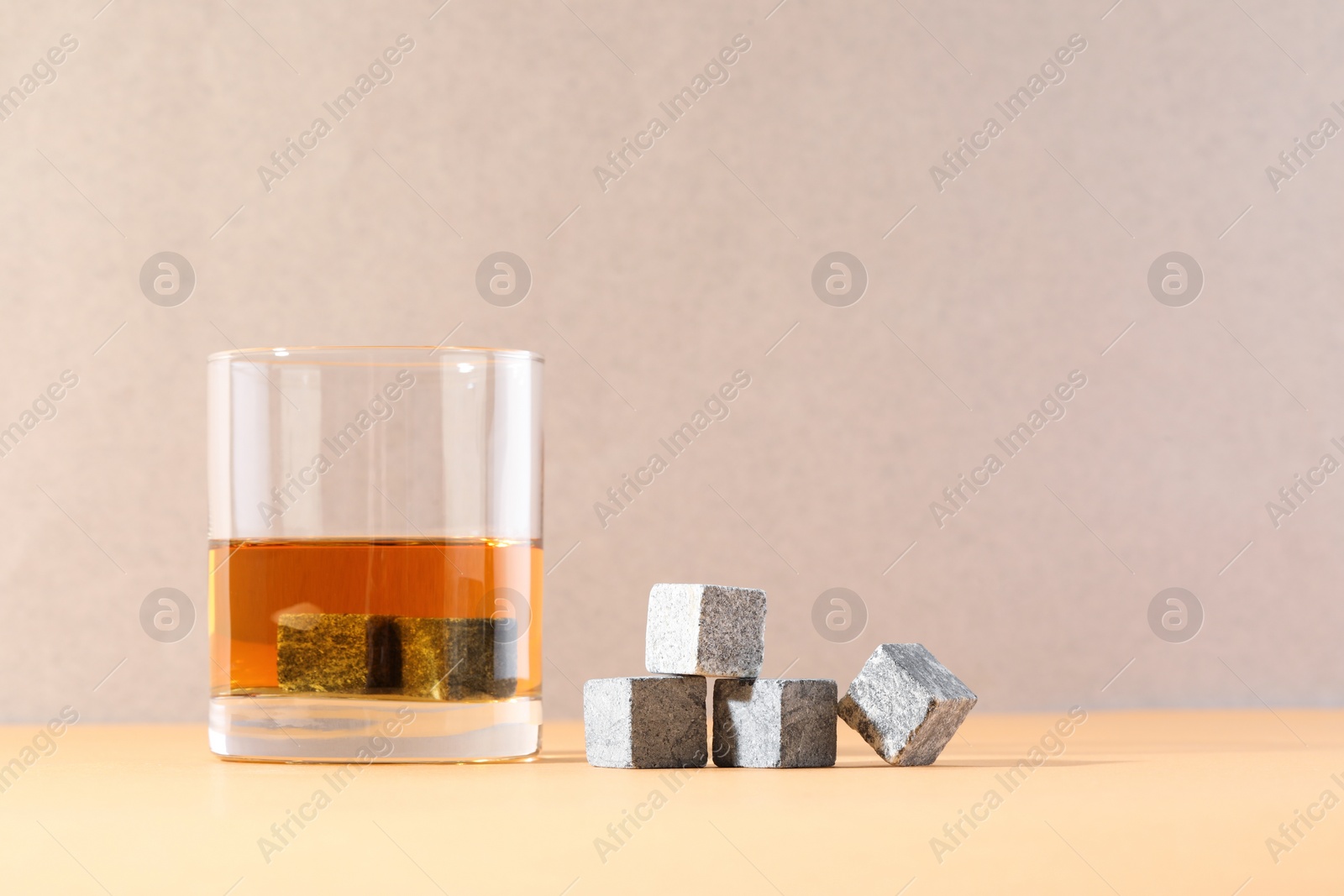 Photo of Whiskey stones and drink in glass on orange table. Space for text