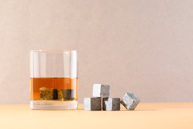 Whiskey stones and drink in glass on orange table. Space for text
