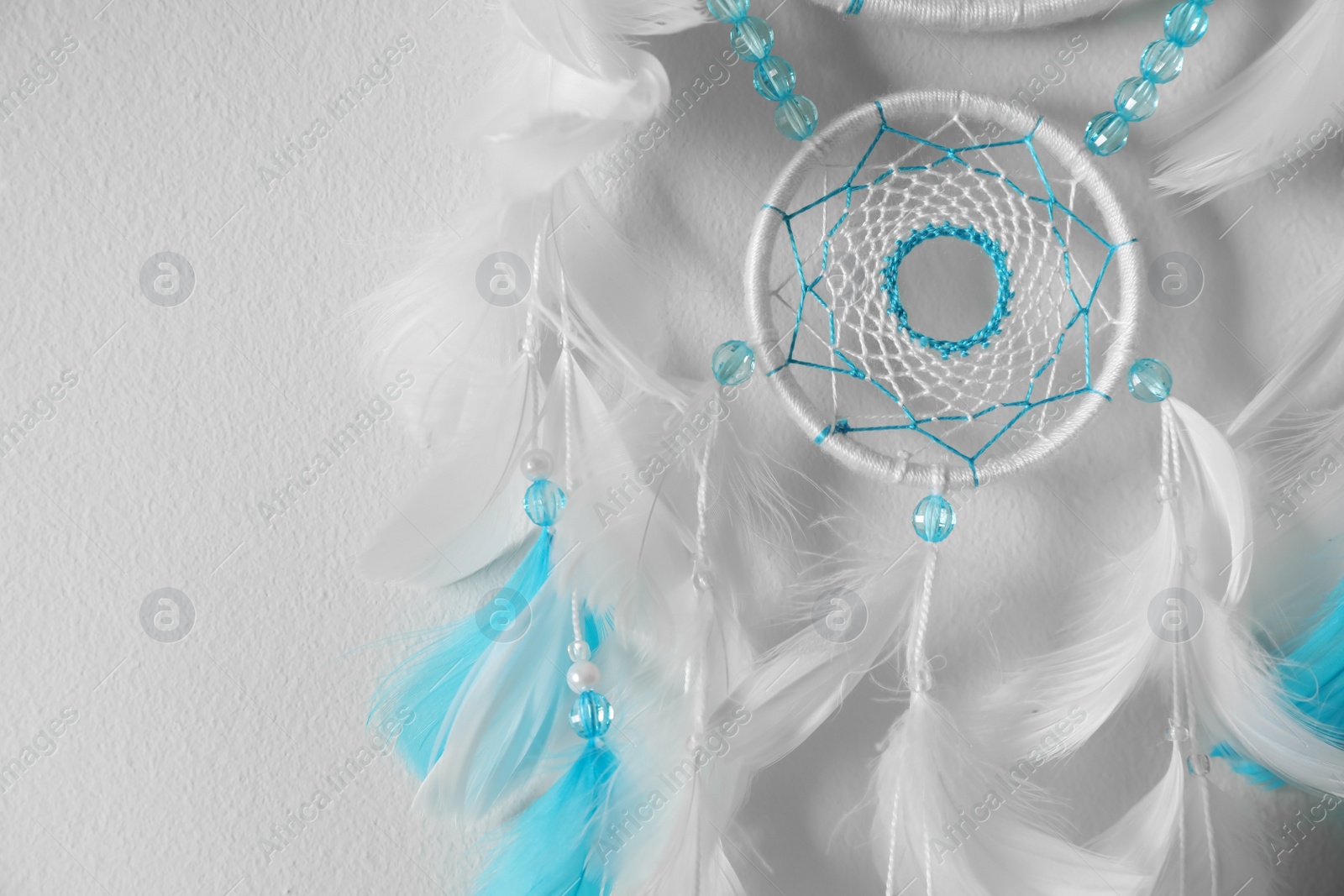 Photo of Beautiful dream catcher hanging on white wall, closeup