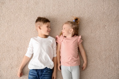 Photo of Cute little children lying on cozy carpet at home, top view