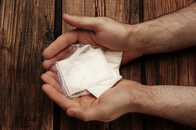 Photo of Man holding plastic bags with cocaine on wooden background, closeup